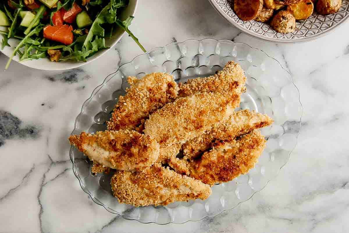 crispy apple honey glazed chicken tenders on plate with roasted potatoes and salad on the side.