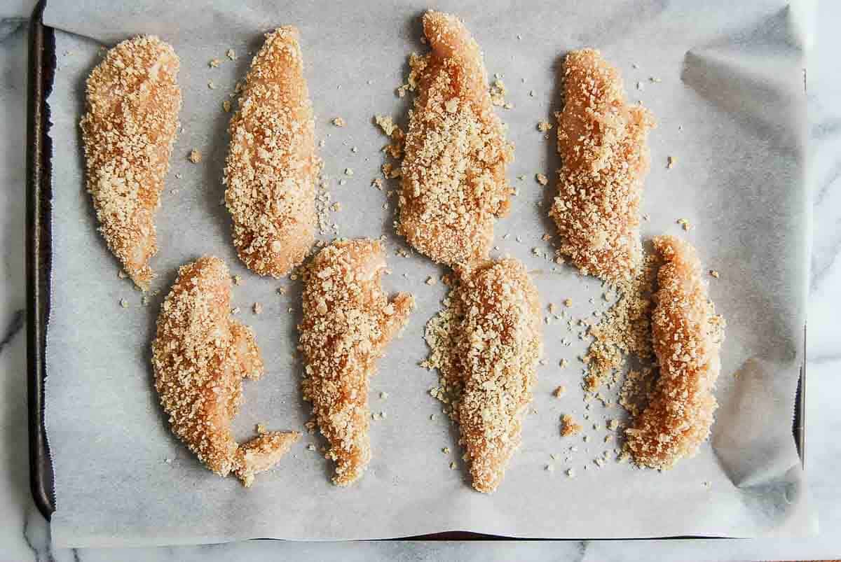 apple and honey glazed chicken tenders dipped in panko breadcrumbs on baking sheet lined with parchment paper.
