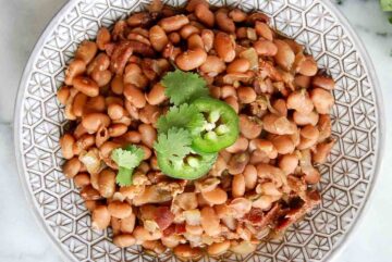 slow cooker pinto beans in serving bowl with cilantro and jalapeno slices on top.