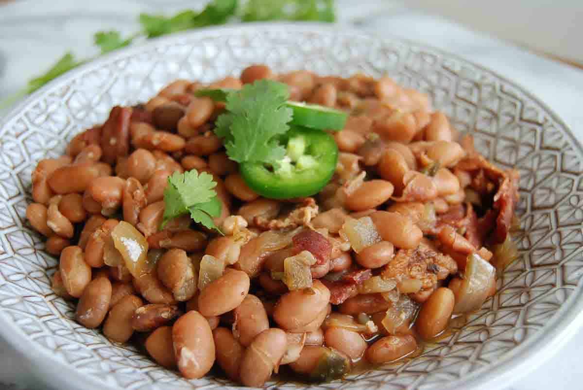 side view of crock pot pinto beans with cilantro and jalapeno pepper slices on top.