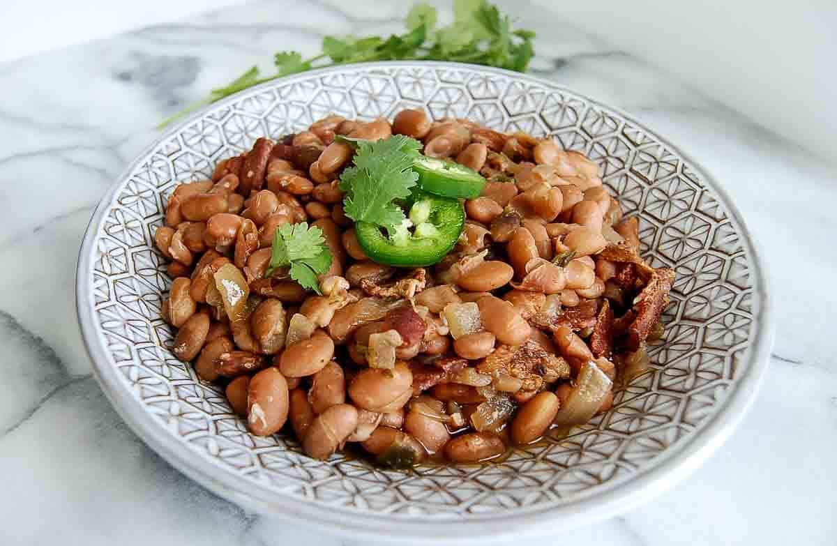 slow cooker pinto beans in serving bowl with cilantro and jalapeno slices on top.