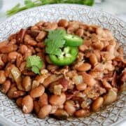 crockpot pinto beans in serving bowl with cilantro and jalapeno slices on top.