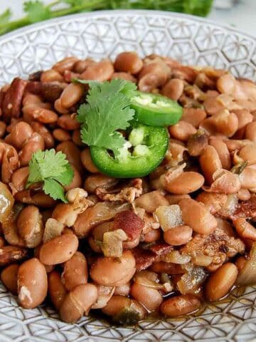 crockpot pinto beans in serving bowl with cilantro and jalapeno slices on top.