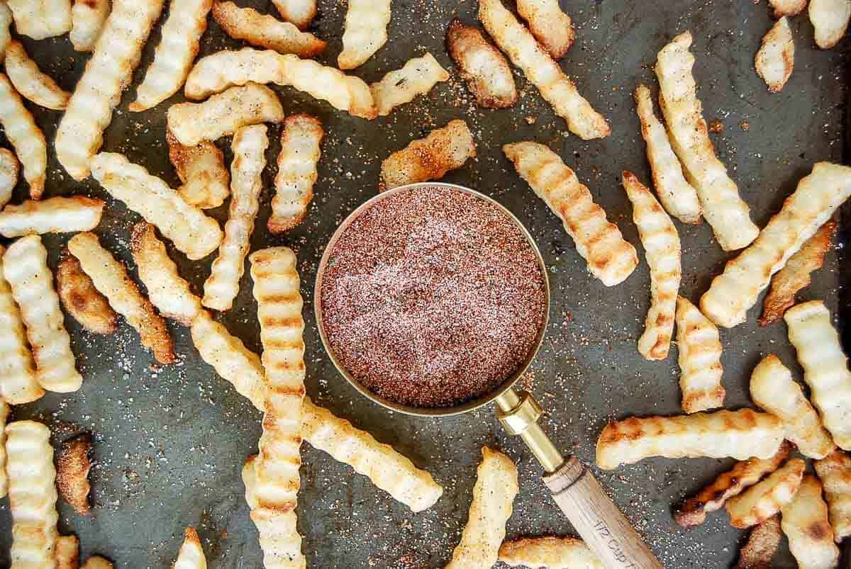 closeup of fry seasoning in measuring cup with seasoned fries scattered around it.