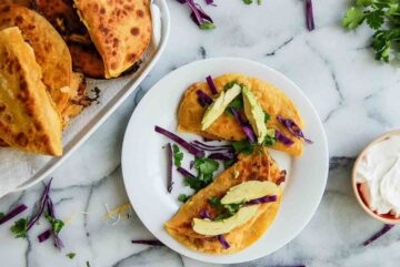 potato tacos on plate with avocado, red cabbage and cilantro.