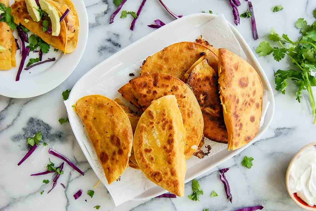 tray of potato tacos with cilantro, red cabbage and sour cream on the side.