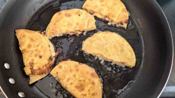 potato tacos frying in pan.