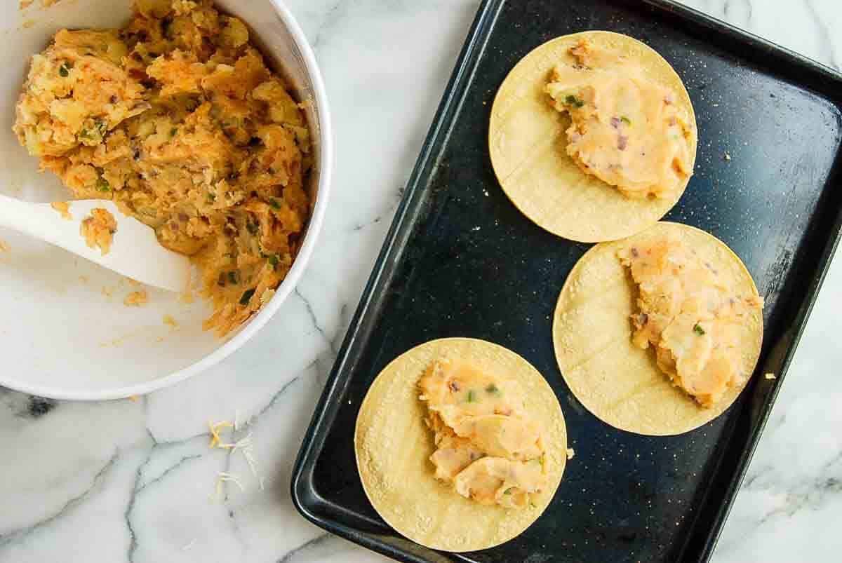 pan with corn tortillas and potato cheese and veggie mixture spread on half.