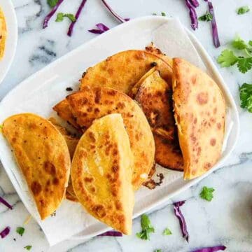 tray of fried potato tacos with cilantro and red cabbage on the side.