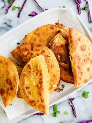 tray of fried potato tacos with cilantro and red cabbage on the side.
