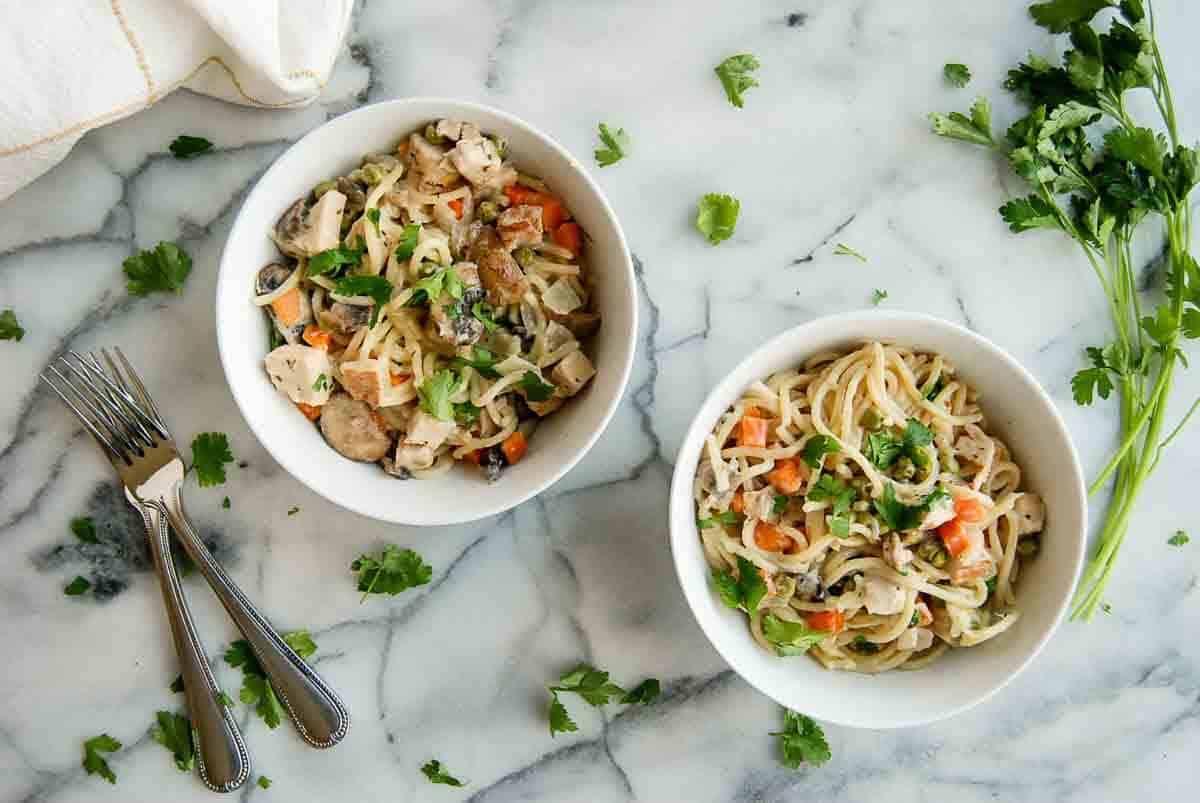 turkey tetrazzini in individual bowls with forks and parsley on the side.