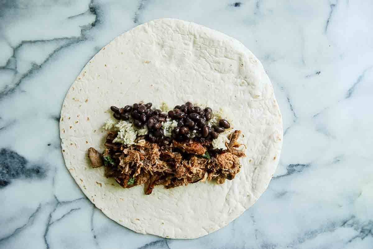 flour tortilla with carnitas, rice and black beans piled on top.