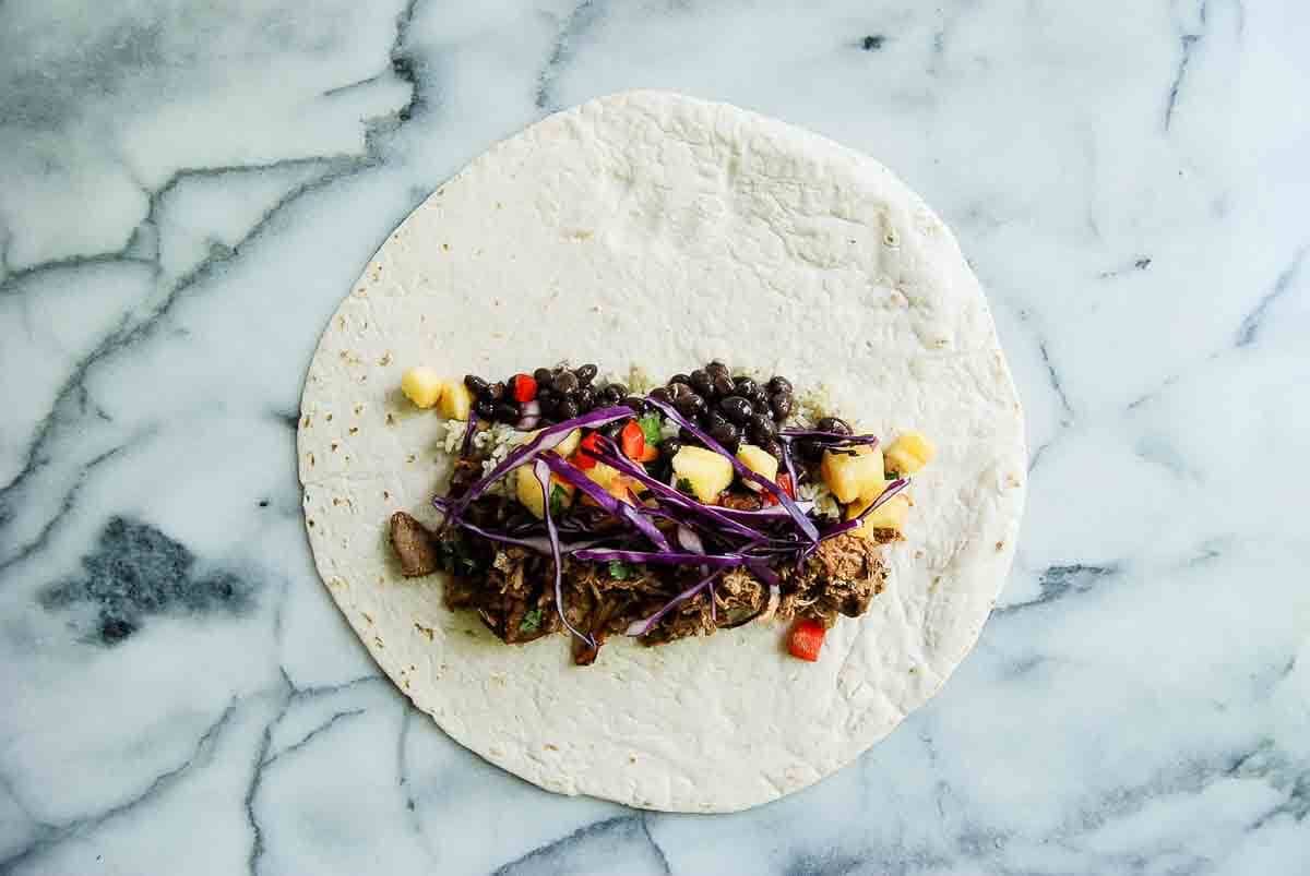 tortilla with carnitas, red cabbage, rice, black beans and pineapple salsa piled on top.