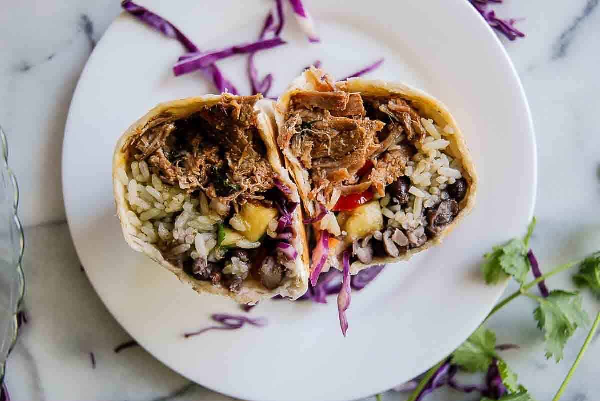carnitas burrito cut in half on plate.