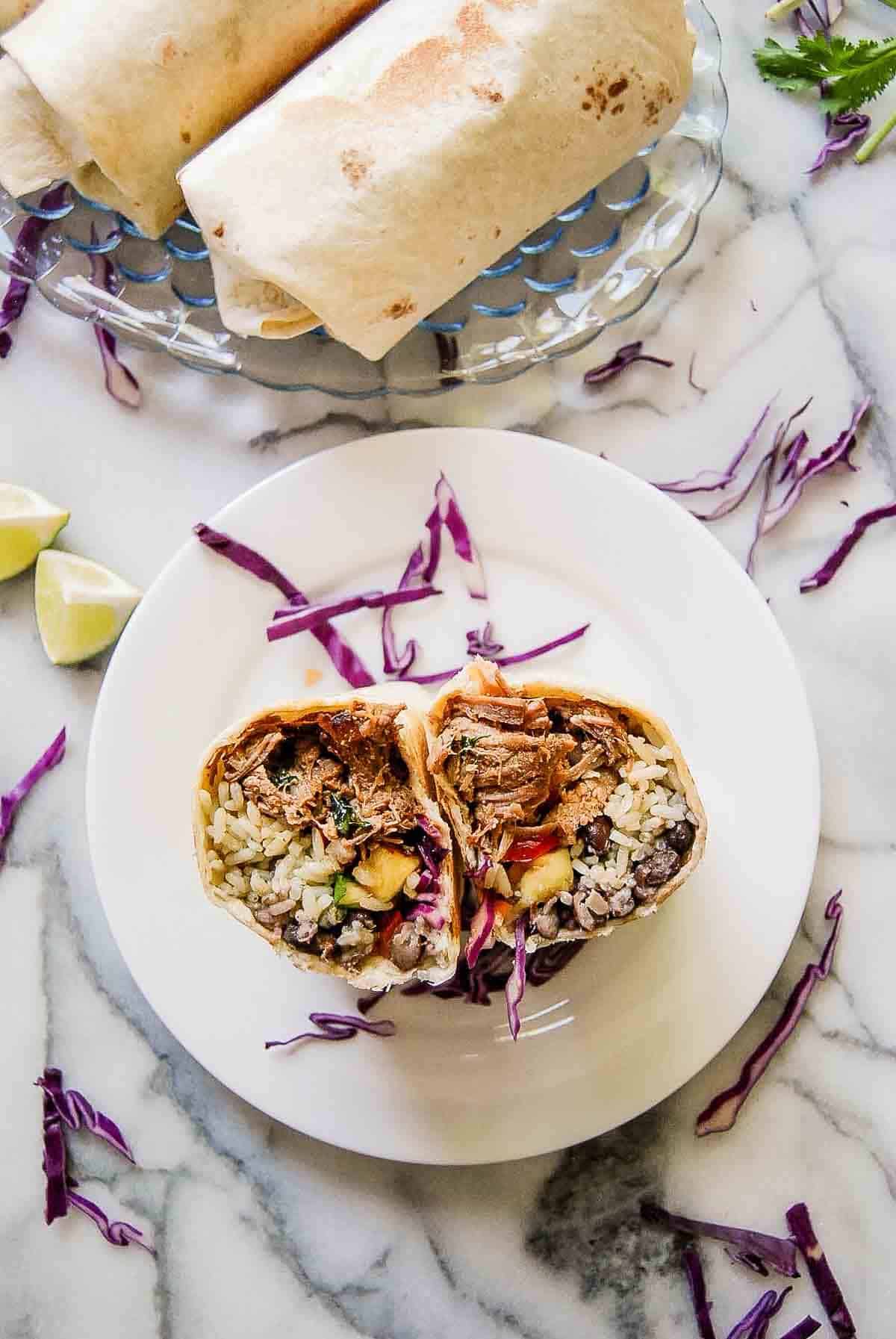 carnitas burrito cut in half on plate with more burritos to the side.