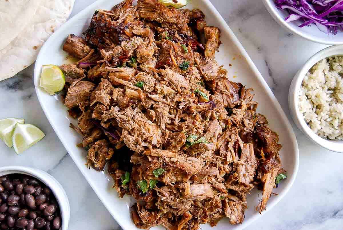 plate full of pork carnitas with burrito ingredients on the side.