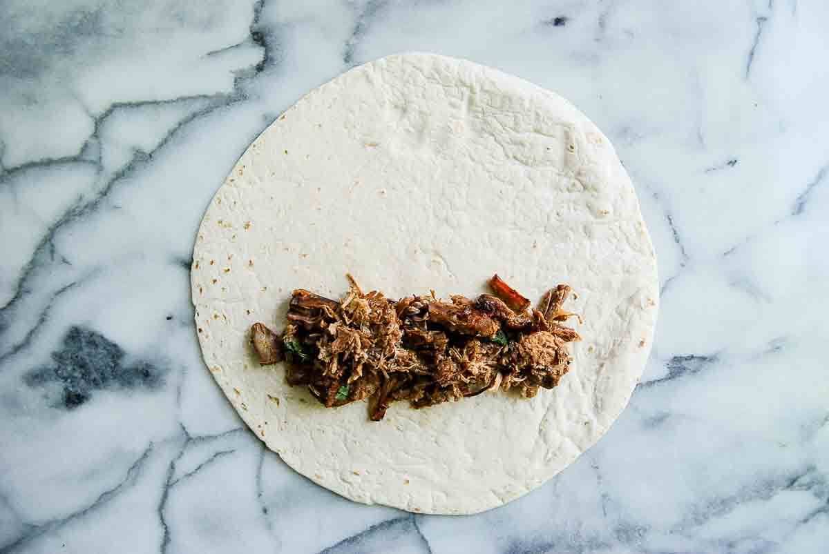 flour tortilla with carnitas piled on top