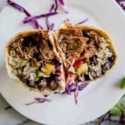pork carnitas burrito cut in half on plate.