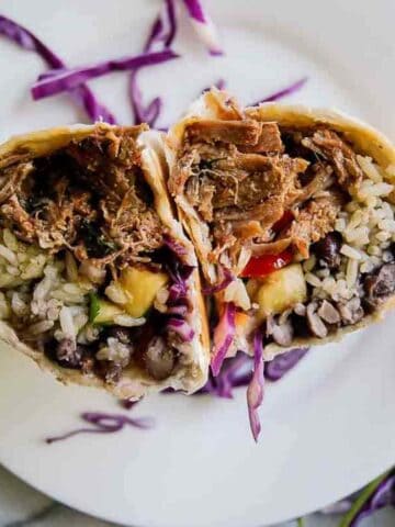 pork carnitas burrito cut in half on plate.