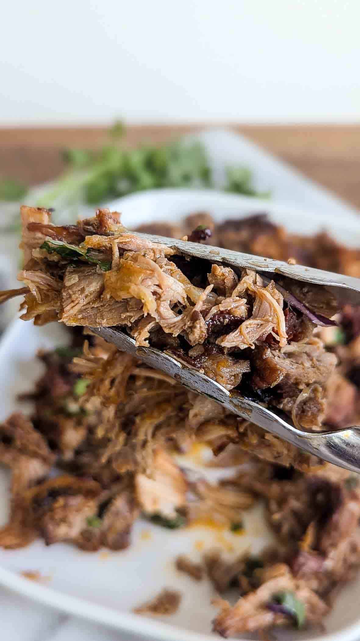 tongs holding pork carnitas.
