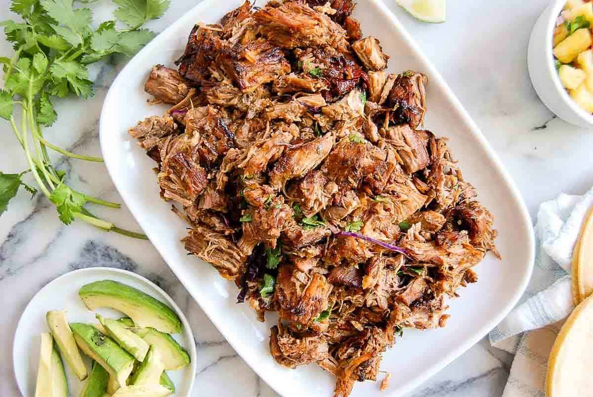 crispy instant pot carnitas on serving platter with avocado and limes on the side.