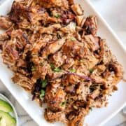 crispy instant pot carnitas on serving platter with avocado and limes on the side.