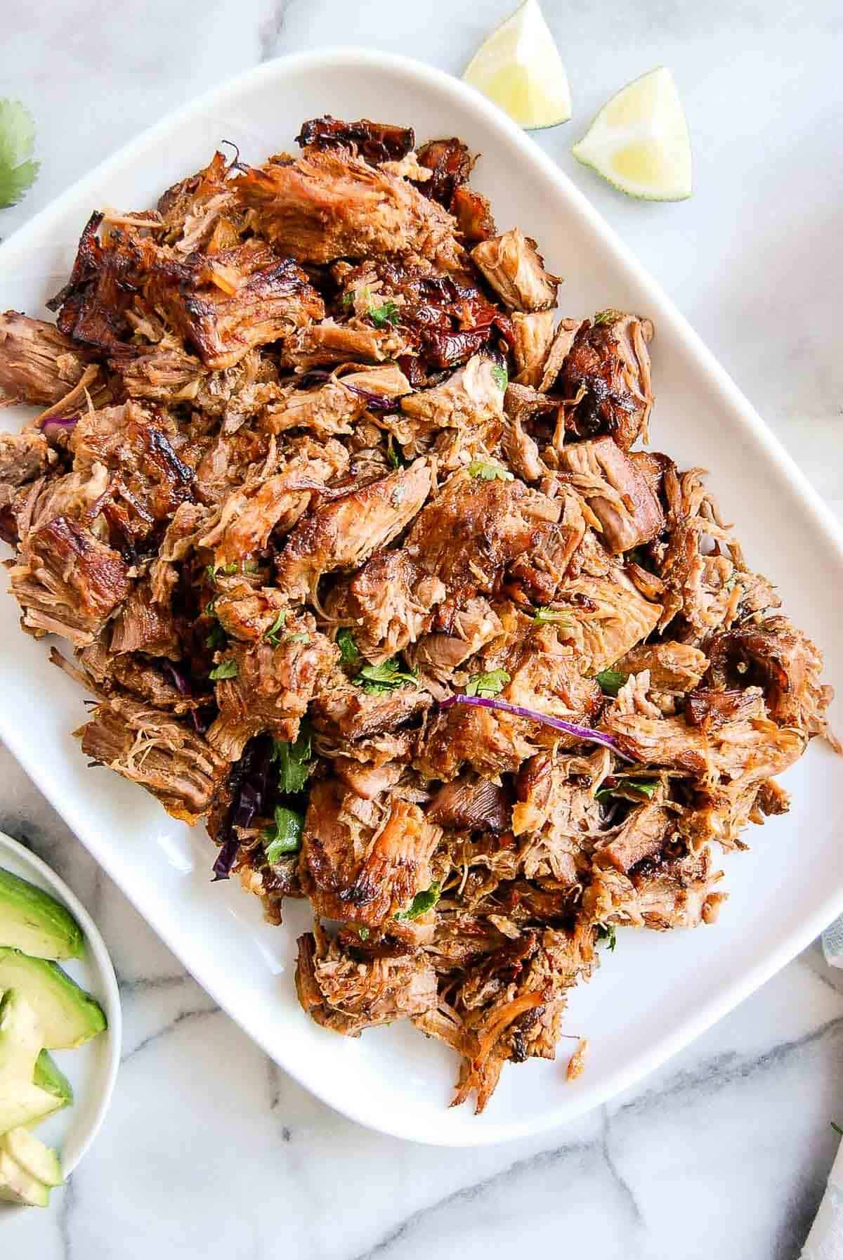 crispy instant pot carnitas on serving platter with avocado and limes on the side.