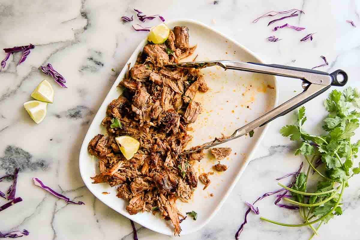 crispy instant pot carnitas on serving platter with half removed and tongs on the side.