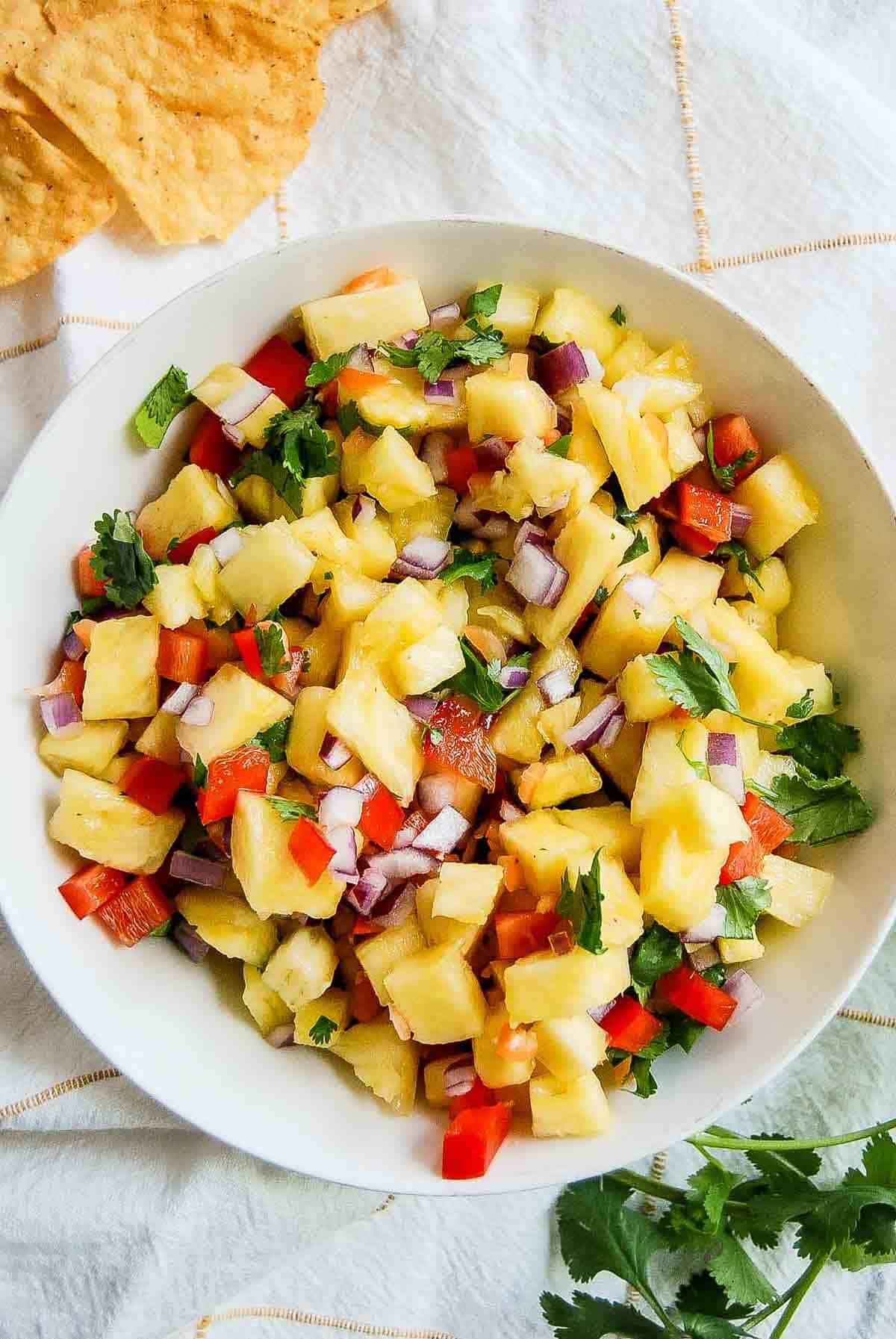 bowl of pineapple salsa with habaneros on countertop with chips scattered around it.