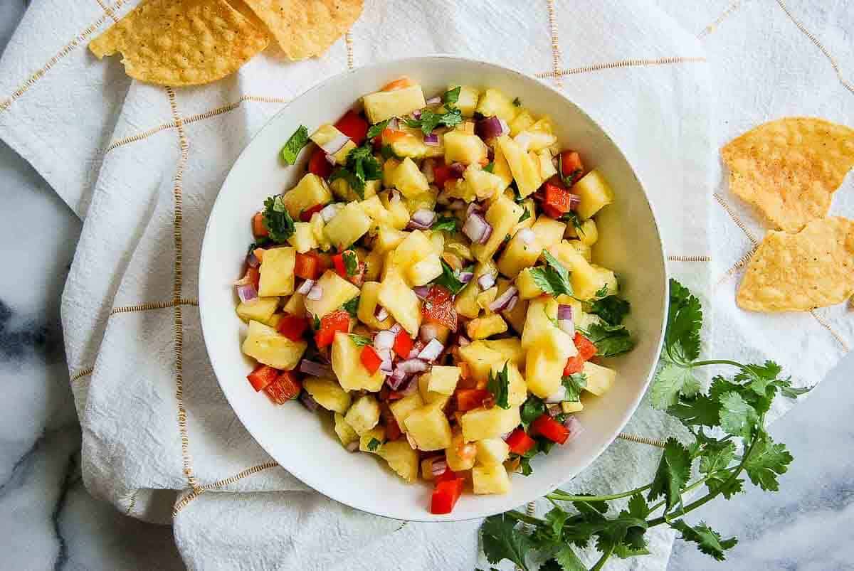bowl of pineapple salsa with habaneros on countertop with chips scattered around it.