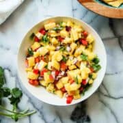 bowl of pineapple habanero salsa on countertop with bowl of chips and cilantro on the side.