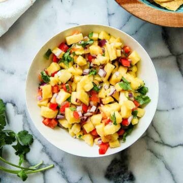 bowl of pineapple habanero salsa on countertop with bowl of chips and cilantro on the side.