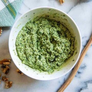 basil walnut pesto in bowl on countertop with wooden spoon and walnuts on the side.