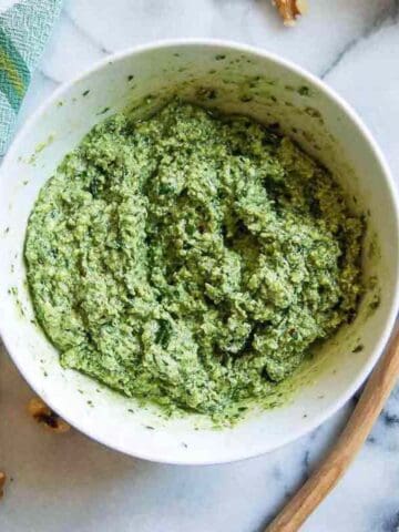 basil walnut pesto in bowl on countertop with wooden spoon and walnuts on the side.