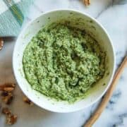 basil walnut pesto in bowl with walnuts and wooden spoon to the side.