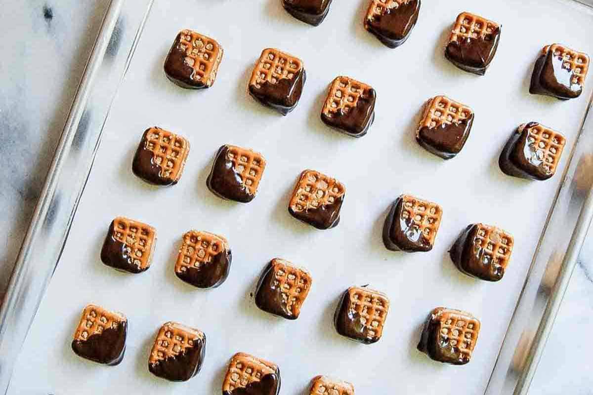 A tray of square pretzels, each half-dipped in chocolate, arranged neatly in rows on a white surface.