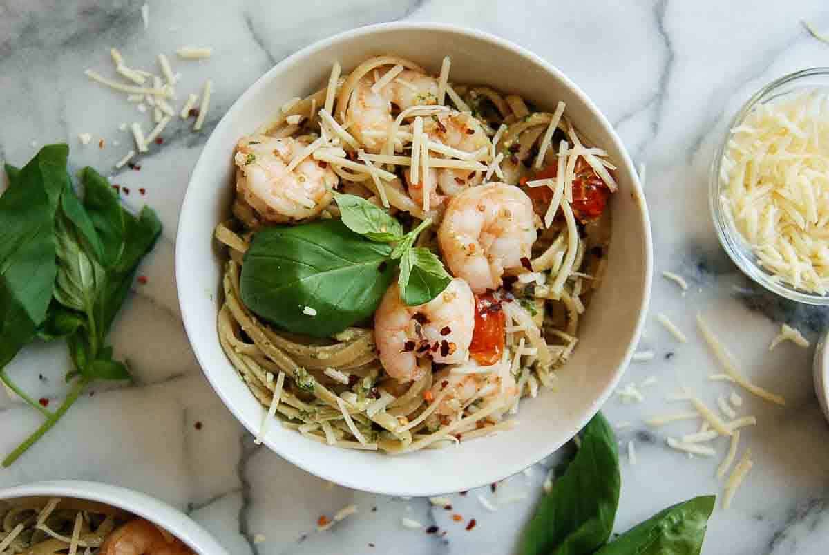 shrimp pesto pasta in bowl with parmesan, basil and red pepper sprinkled on top.