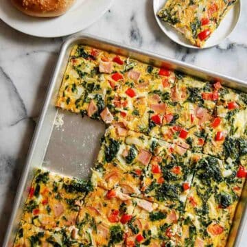 Fresh vegetable and ham breakfast casserole with spinach, red peppers, and cheese on a baking sheet. separately to the side.