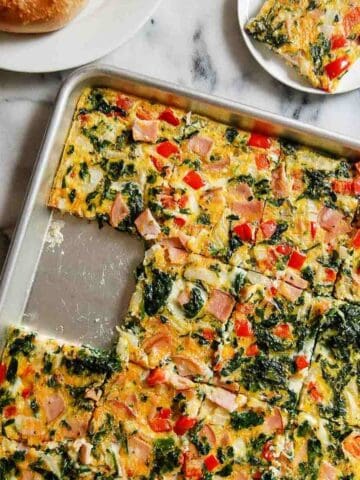 Fresh vegetable and ham breakfast casserole with spinach, red peppers, and cheese on a baking sheet. separately to the side.
