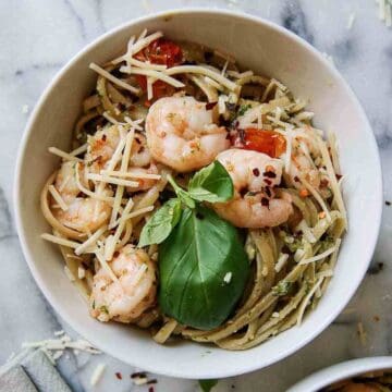 shrimp pesto pasta in bowl on countertop with parmesan, basil and red pepper sprinkled on top.