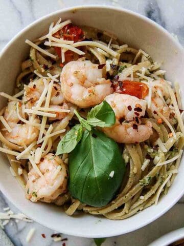 shrimp pesto pasta in bowl on countertop with parmesan, basil and red pepper sprinkled on top.