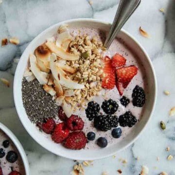 Side view of banana, and mixed berry smoothie bowl with chia seeds, coconut flakes and granola.