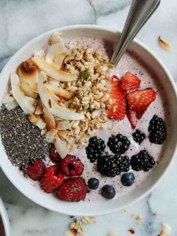 Side view of banana, and mixed berry smoothie bowl with chia seeds, coconut flakes and granola.