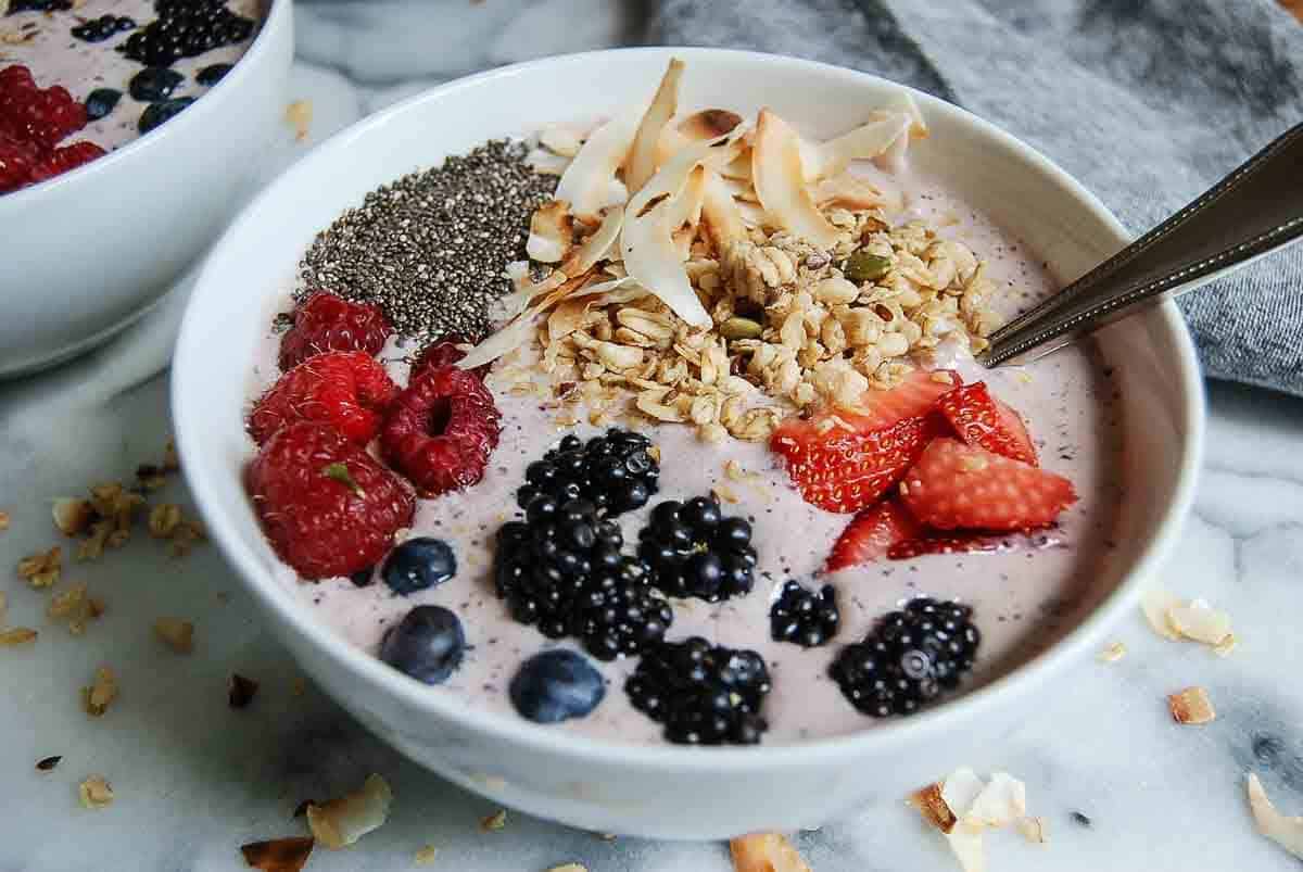 side. view of banana, and mixed berry smoothie bowl with chia seeds, coconut flakes and granola.
