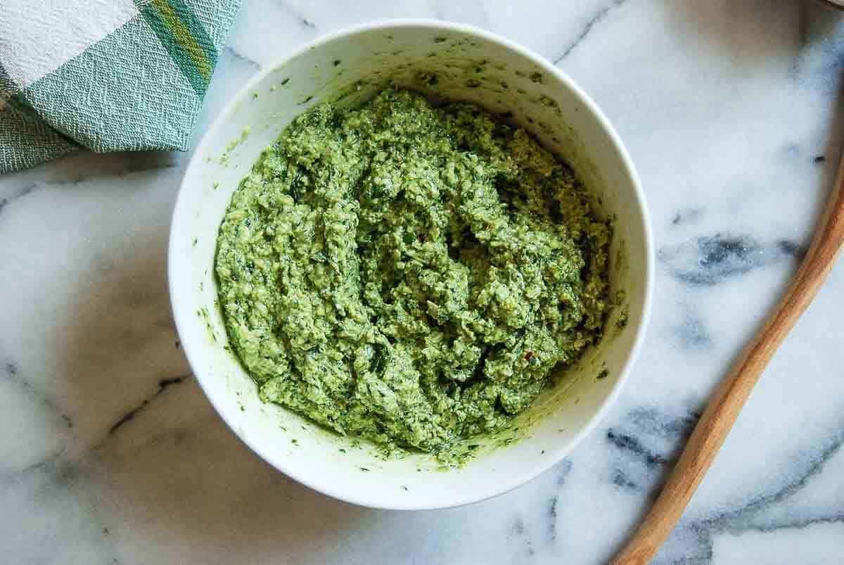 basil walnut pesto in bowl on countertop with olive oil stirred in.