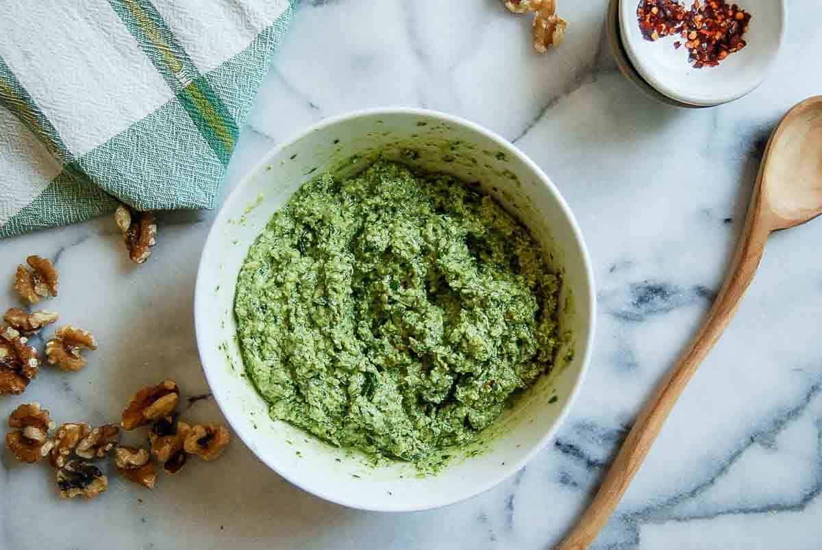 basil walnut pesto in bowl on countertop with spoon and walnuts on the side.