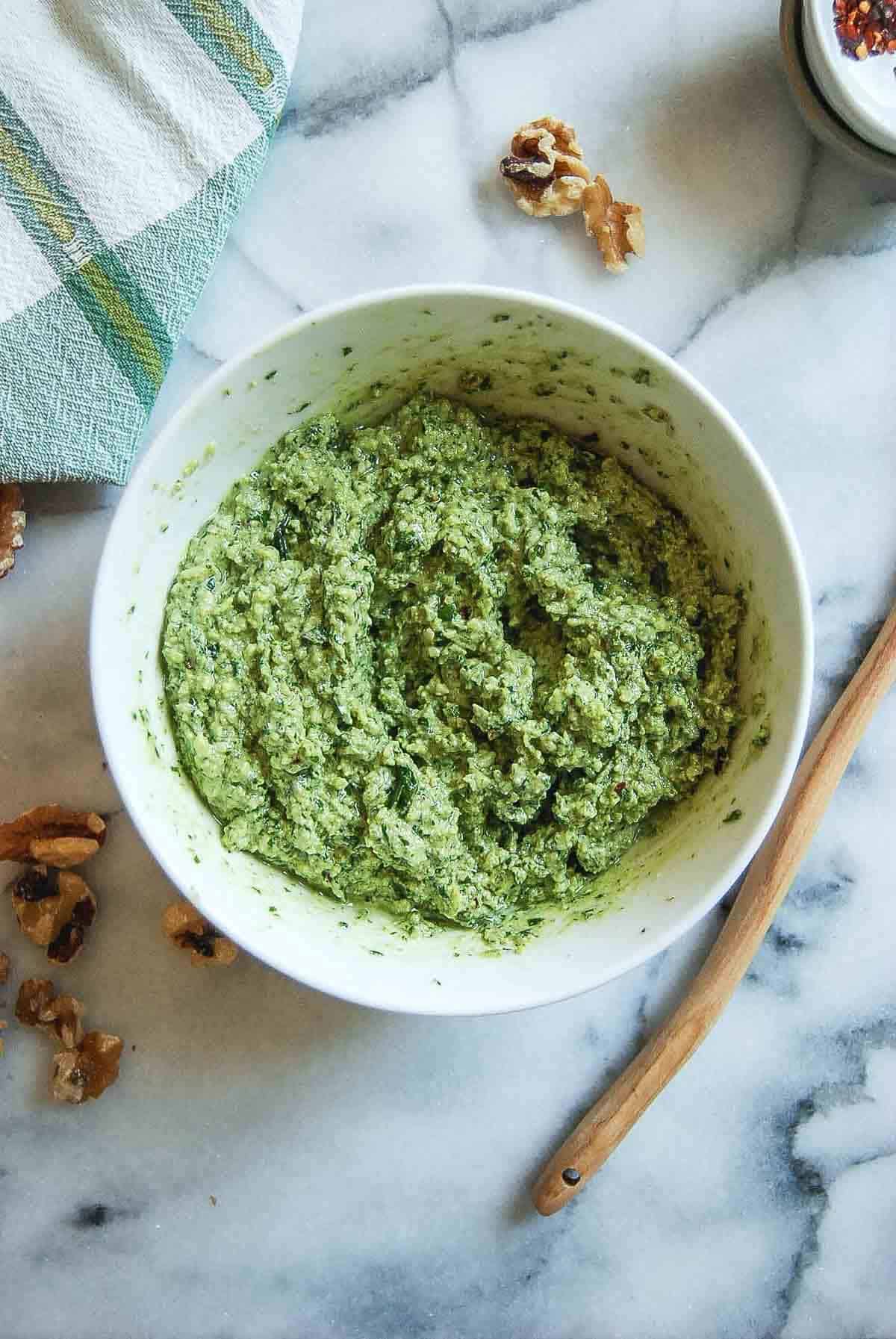 basil walnut pesto in bowl on countertop with spoon and walnuts on the side.
