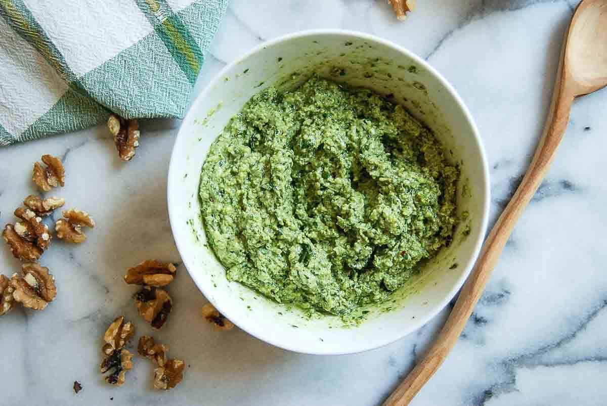 basil walnut pesto in bowl on countertop with spoon and walnuts on the side.