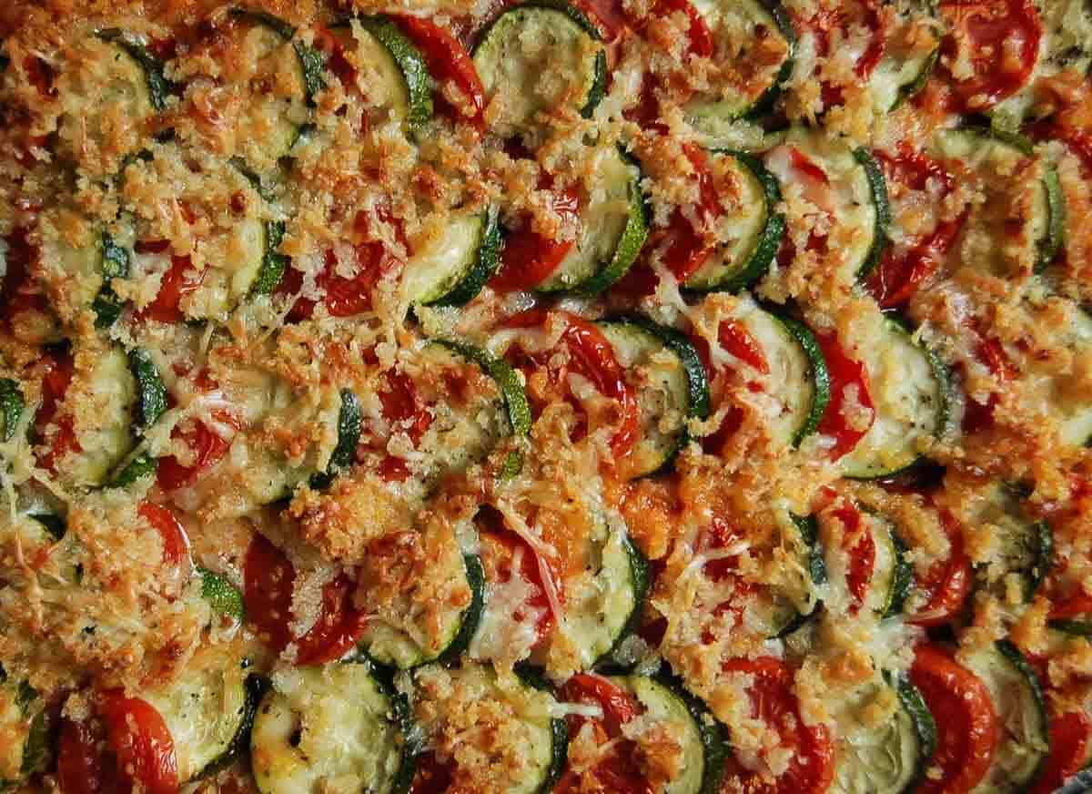 Sliced zucchini and tomatoes layered in a baking dish, topped with melted cheese, breadcrumbs, and herbs, creating a colorful, crispy baked vegetable casserole.
