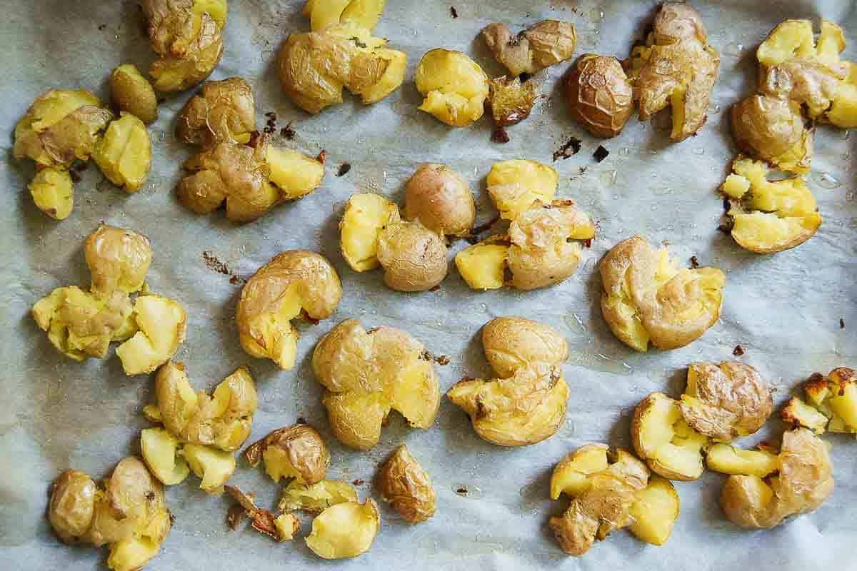 Golden-brown smashed potatoes scattered on a parchment-lined baking sheet, with crispy edges and slightly cracked, fluffy interiors.